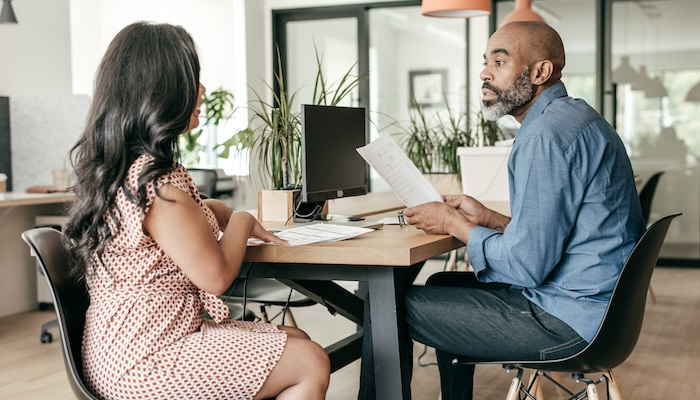 Man and woman sitting at table while discussing documents.