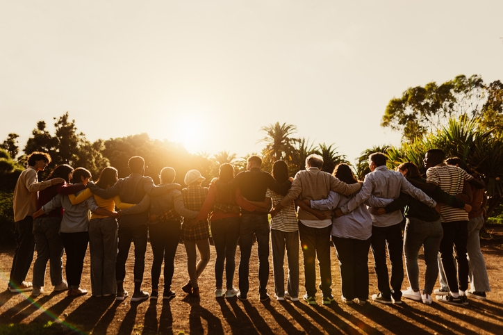 A group of people standing together with their arms around each other, looking towards the sunlight.