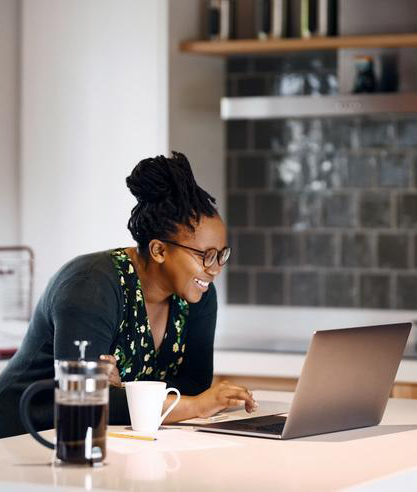 Smiling woman in a modern kitchen, looking at her laptop while enjoying a cup of coffee, suggesting she is checking finances.